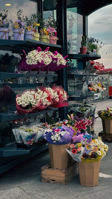 A display of various floral arrangements at an outdoor flower shop, featuring bouquets of fresh flowers including white daisies, pink lilies, and purple asters wrapped in colorful paper and placed in 