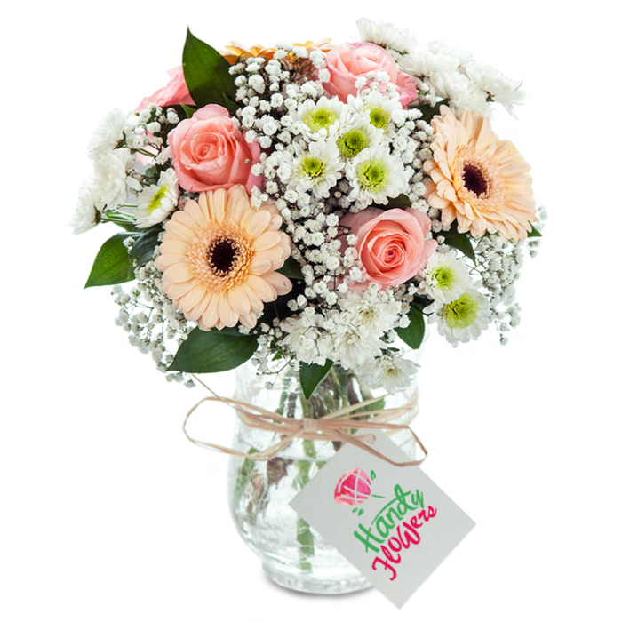 Nestled in a sun-dappled corner reminiscent of Ealing's inviting residential streets, this lush bouquet brims with locally sourced freshness and artistry. Central to the design are classic peach-pink roses, their petals unfurling with velvety luxury and capturing the timeless romance felt beside the duck ponds of Walpole Park. Two lively peach-orange gerberas provide a contemporary twist with their wide, flawless petals and distinctive deep brown centres, invoking the cheerful mood of Saturday mornings near Ealing Green. Crisp white chrysanthemums, flecked with lime green at the heart, and an abundance of frothy baby's breath intermingle throughout, lending the arrangement a harmonious sense of movement and volume. Strategically interwoven sprigs of deep green eucalyptus catch the light and add depth, while their cool scent hints at freshly picked botanicals. The flowers are presented in a clear glass vase-stems and fresh water visible-tied with a slim, rustic raffia bow, reflecting the neighbourhood's understated yet refined tastes. From the bow hangs a simple, contemporary white gift tag, thoughtfully left uninscribed and ready for your own message. Every detail, from the fullness of the blooms to the artisanal ribbon, signals the careful attention of a local florist attuned to Ealing's blend of tradition and modernity. Perfect for celebrating milestones, sending heartfelt wishes, or simply brightening a family table in South Ealing, this bouquet is a testament to floral craftsmanship nurtured in the community.